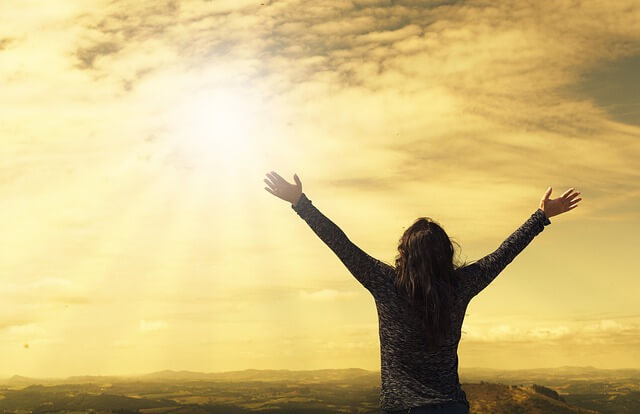 太陽に向かって手を広げる女性